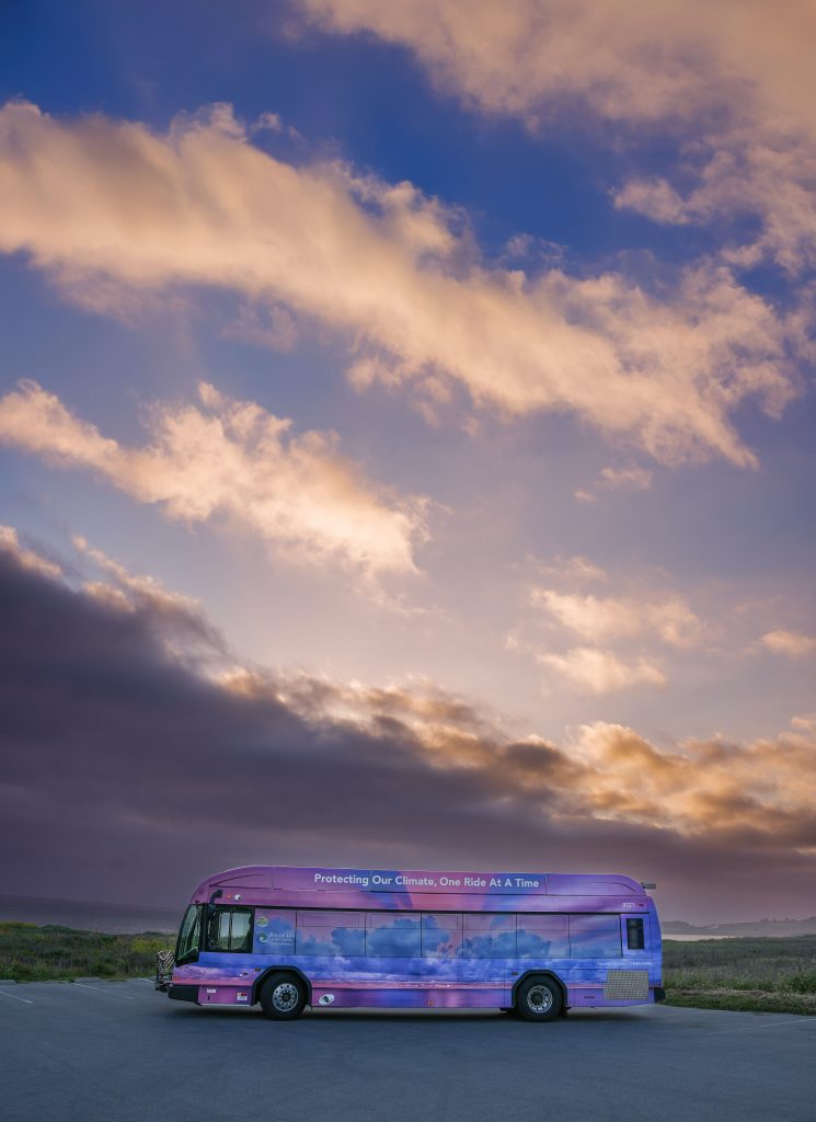 One ride art a Time sunset bus parked in lot at the beach with sunset behind it