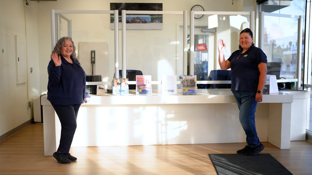 Women standing and waving in front of customer service desk with Headways magazine and different brochures 