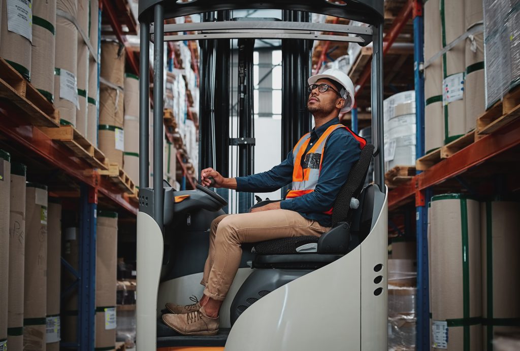Forklift driver focused on carefully transporting stock from shelves around the floor of a large warehouse